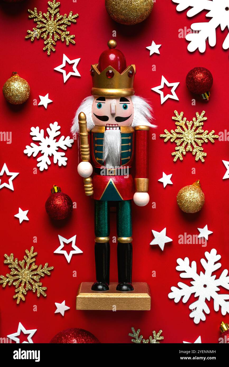 Hintergrund des Weihnachtskonzepts. Blick von oben auf weihnachtlichen hölzernen Nussknacker-Spielzeugsoldat mit weihnachtskugeln, Schneeflocken und weißen Sternen auf rotem Hintergrund Stockfoto