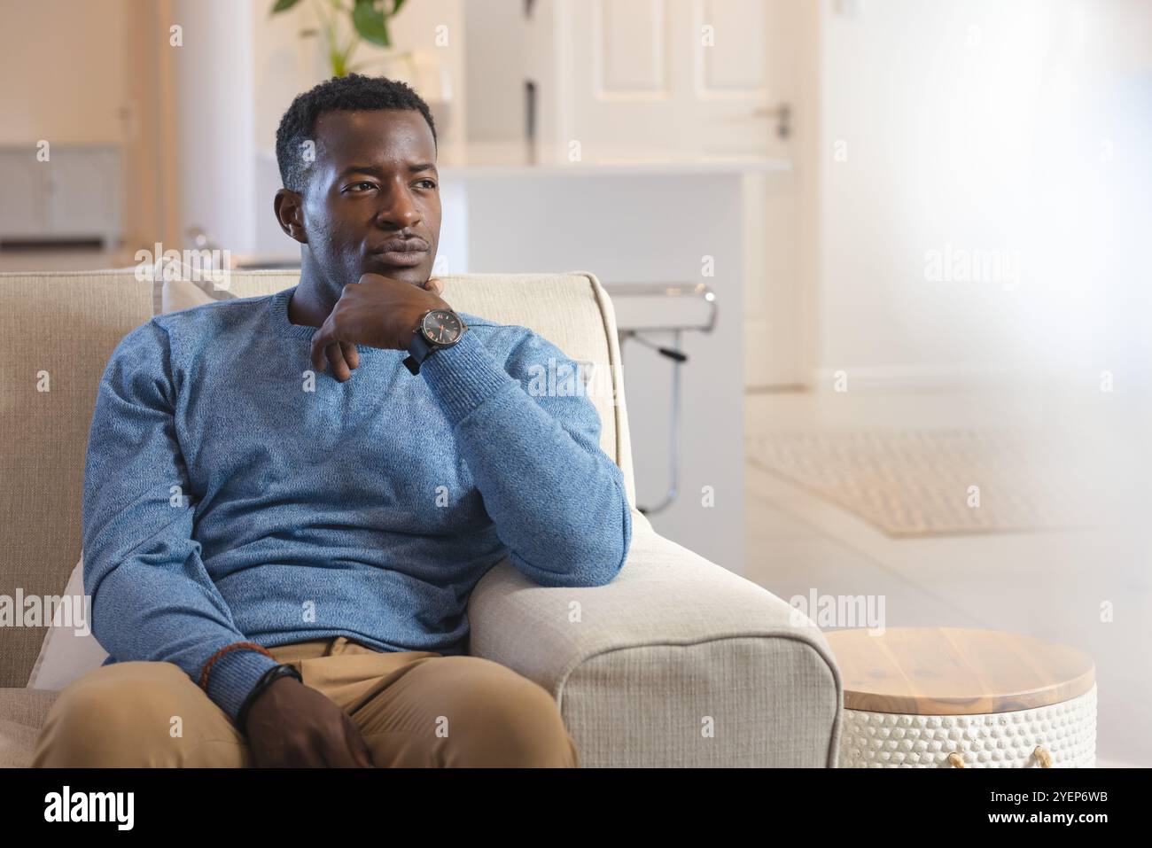 Nachdenklicher afroamerikanischer afroamerikanischer Mann, der sich zu Hause auf dem Sofa entspannt und einen blauen Pullover trägt. Entspannung, Ruhe, gemütlich, drinnen, Lifestyle, le Stockfoto