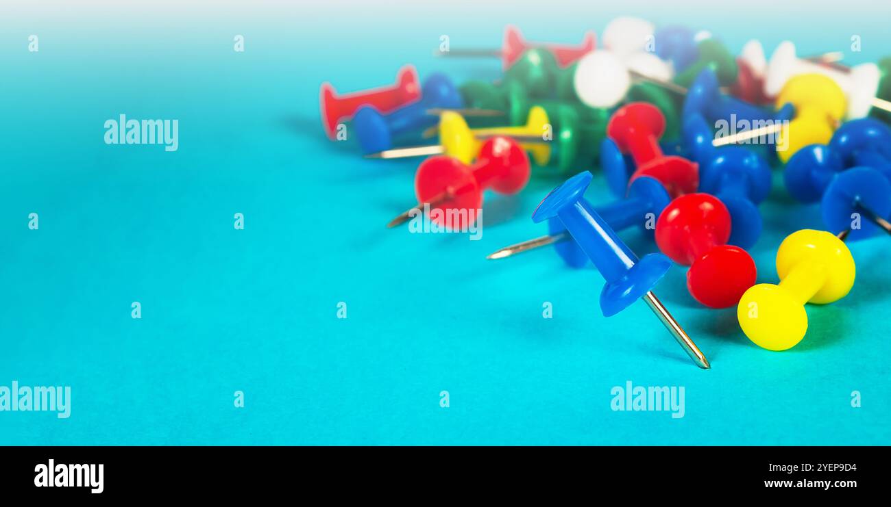 Eine Sammlung von mehrfarbigen Stecknadeln, die auf einer blauen Oberfläche verstreut sind und leuchtende Rot-, Blau-, Gelb- und Grüntöne zeigen, die Organisation symbolisieren Stockfoto