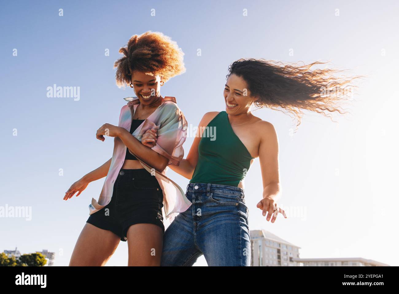 Energiegeladene junge Freunde genießen einen unbeschwerten Tag, tanzen und lachen unter der Sonne. Halten Sie fröhliche und offene Momente in einer fröhlichen Umgebung im Freien fest. Stockfoto