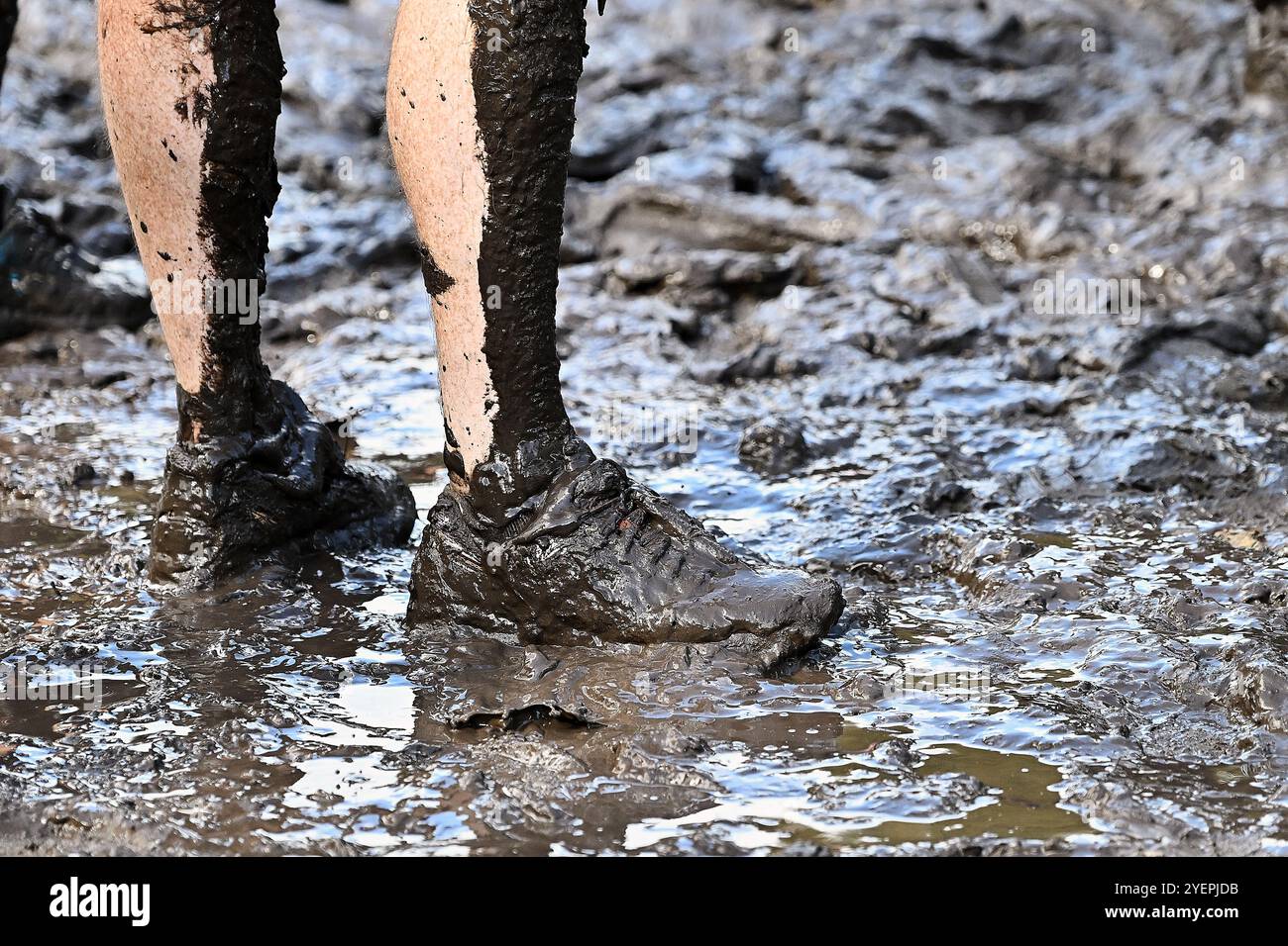 Zwei Beine mit Schuhen auf einem Schlammweg, die von vielen Läufern zertrampelt wurden Stockfoto