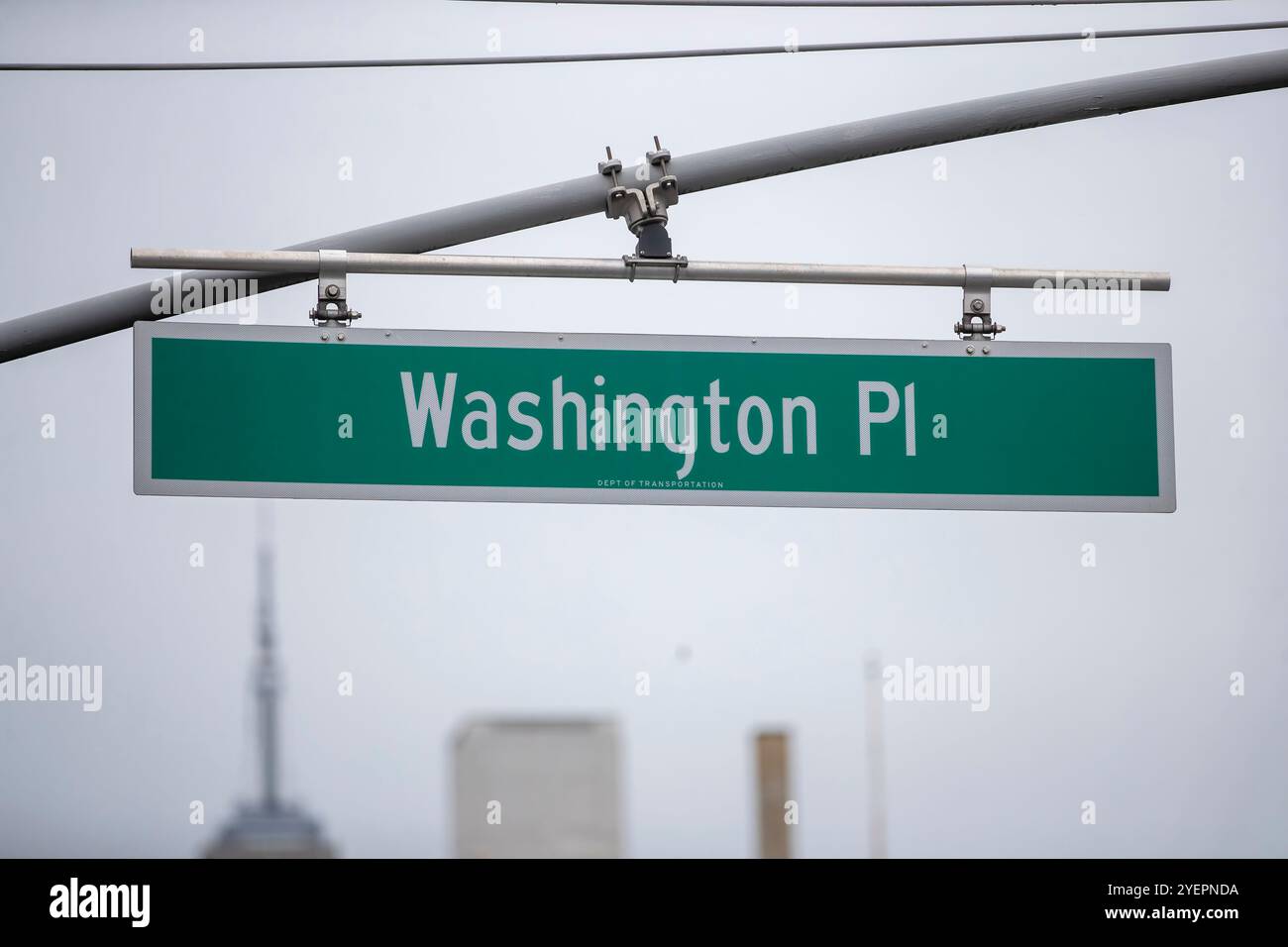 Dieses Bild zeigt eine Nahaufnahme eines grünen Straßenschildes für „Washington PL“ vor einem gedämpften, bedeckten Himmel. Stockfoto