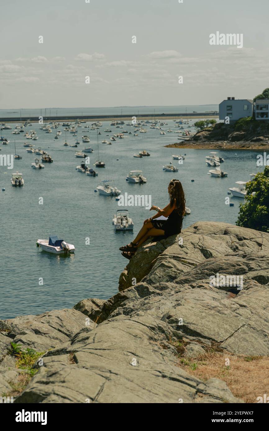 Frau sitzt auf Felsen am Yachthafen an warmen sonnigen Tagen Stockfoto