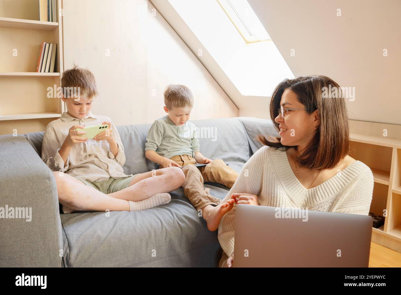 Die Frau arbeitet von zu Hause aus, und die Kinder spielen am Telefon Stockfoto