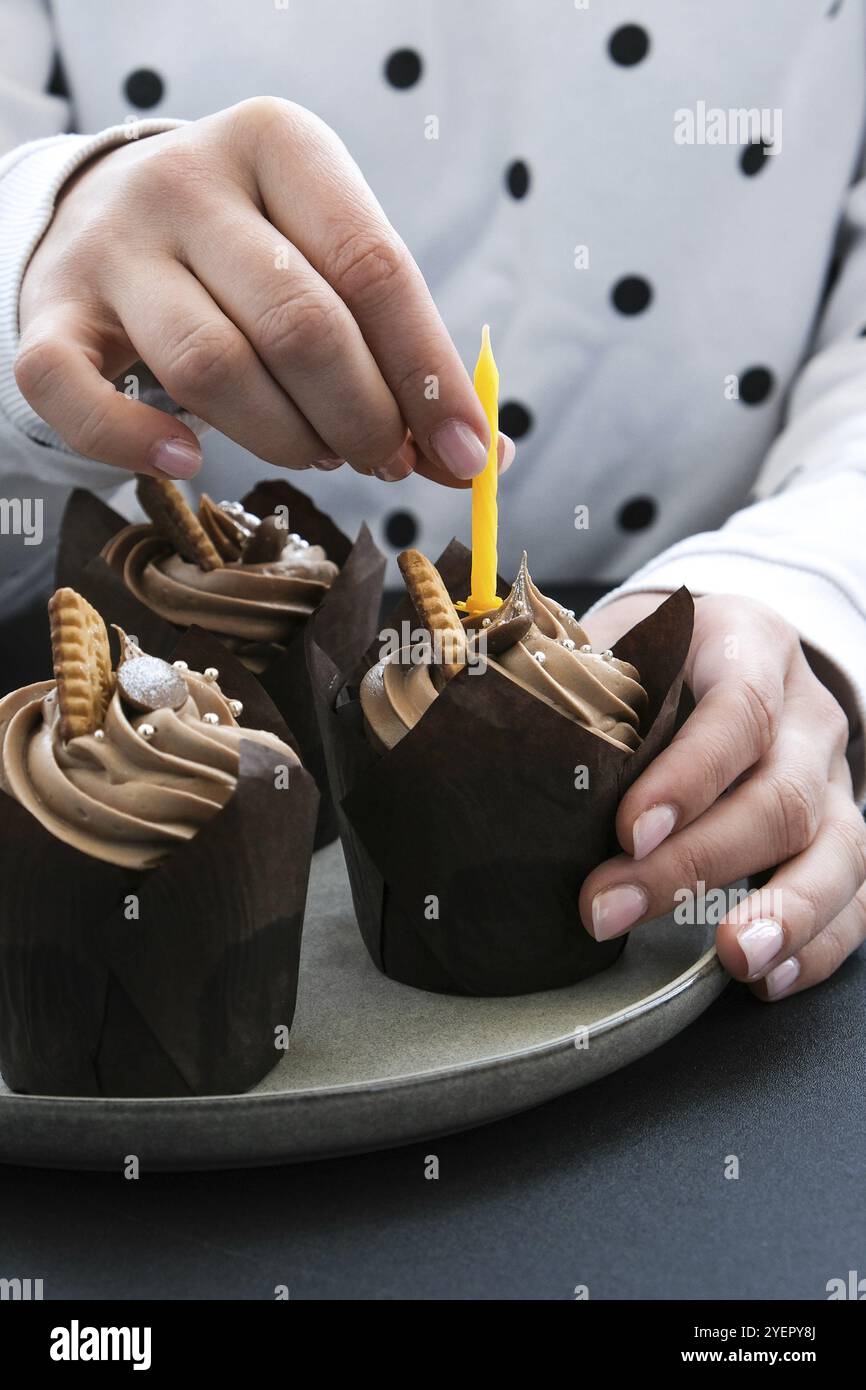 Weibliche Hände, die leckere Cupcakes aus Schokolade mit Creme auf dunklem Hintergrund herstellen. Drei Schokoladenmuffin. Geburtstagskuchen Party Vorbereitung. Hausgemachte Schokolade Stockfoto