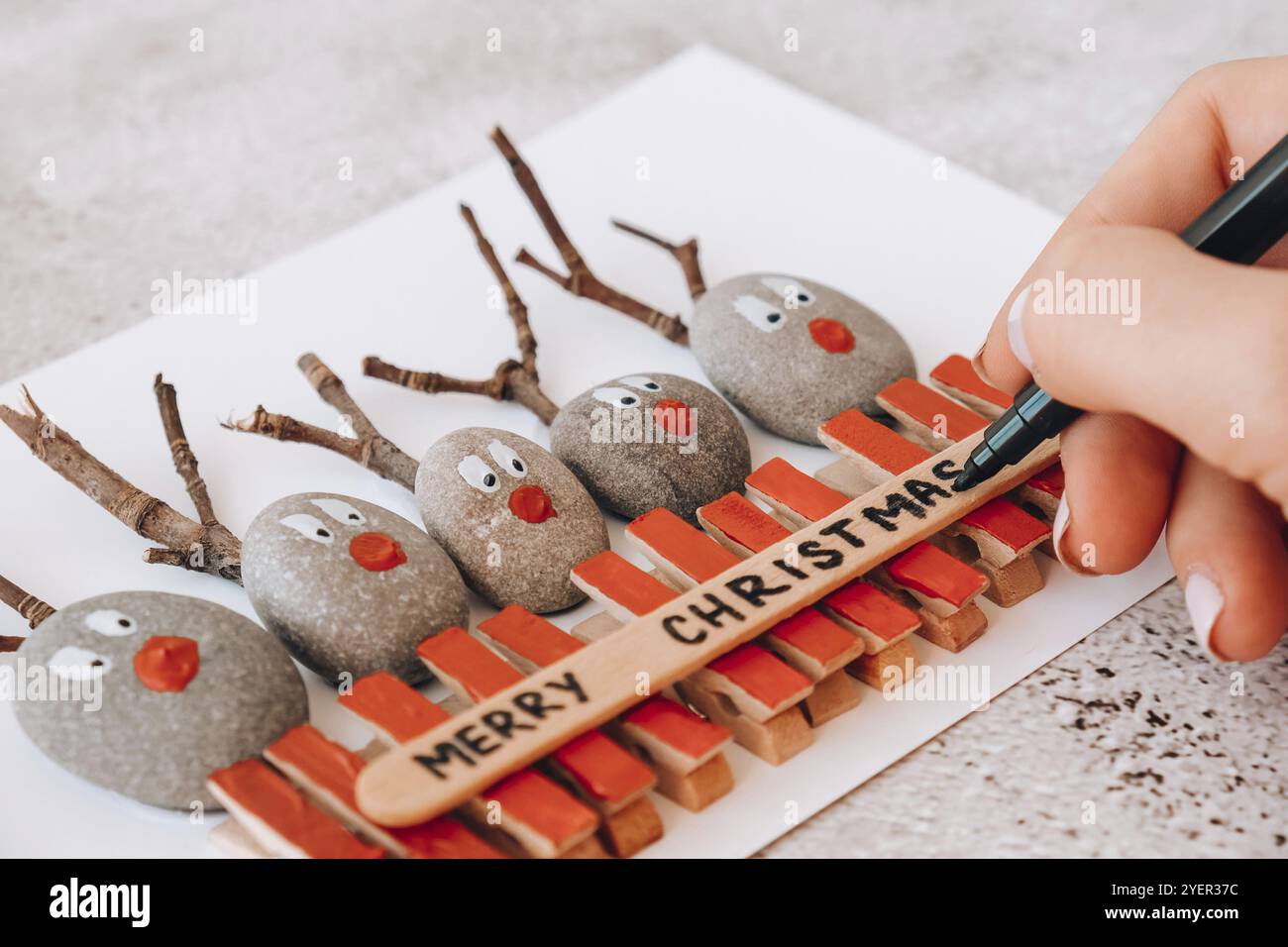 Schritt für Schritt. Draufsicht. Prozess Kinder Handwerk. Do it yourself Fröhliche Weihnachtshirsche auf Grußkarten-Postkarte aus Kieselsteinen, Seesteinen, Klo Stockfoto