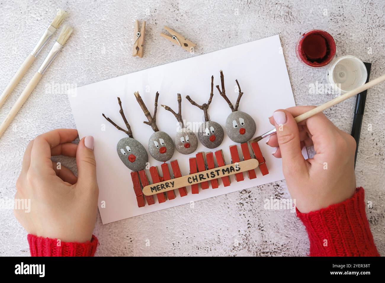 Schritt für Schritt. Draufsicht. Prozess Kinder Handwerk. Do it yourself Fröhliche Weihnachtshirsche auf Grußkarten-Postkarte aus Kieselsteinen, Seesteinen, Klo Stockfoto