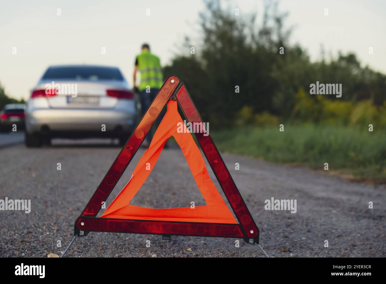 Gebrochenes Silber Luxusauto Notfall Unfall. Man-Fahrer mit rotem Dreieck-Stoppschild auf der Straße. Sportautomat mit Blinkern technische Prüfung Stockfoto