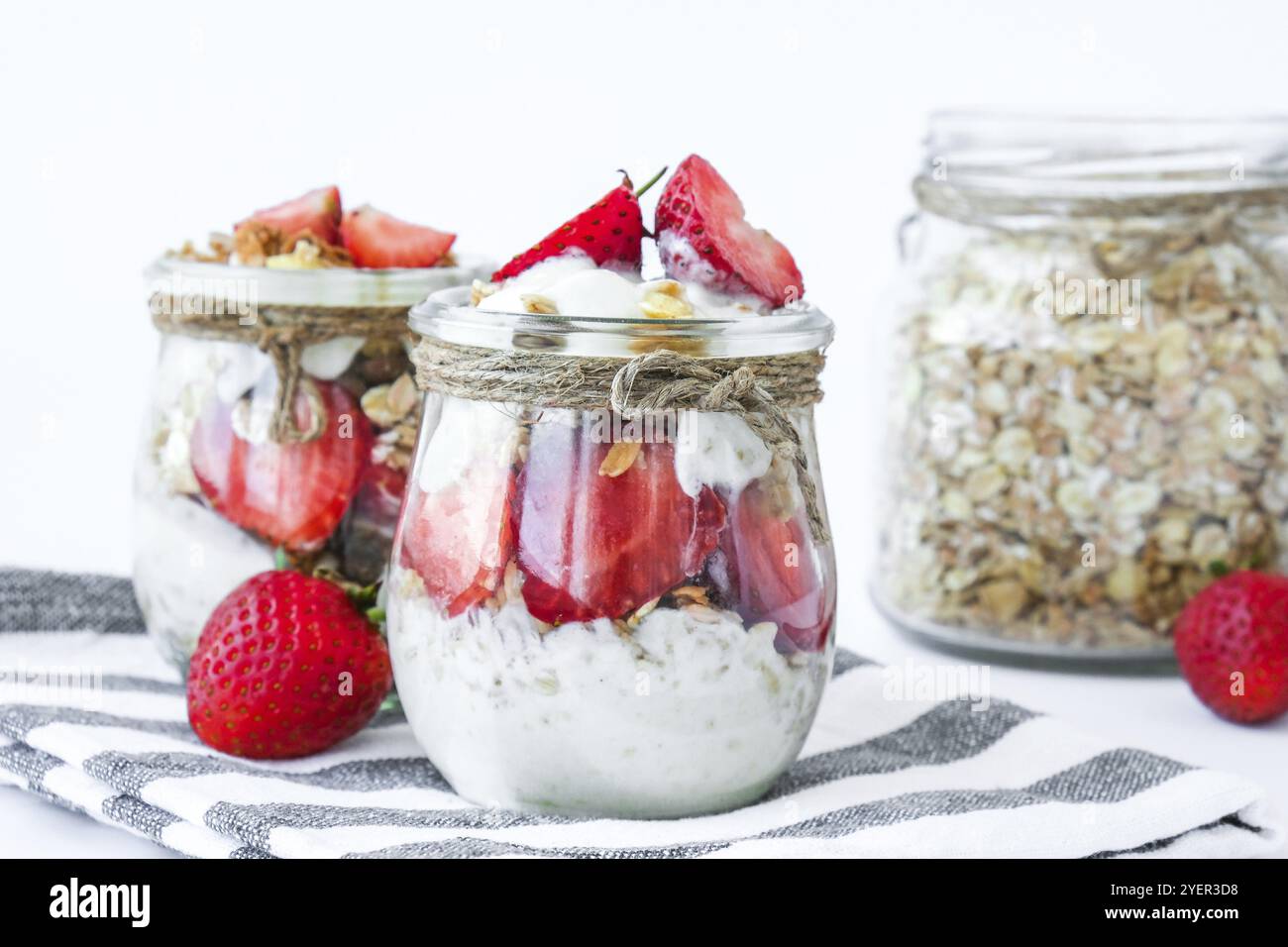 Gesundes Frühstück. Haferflockengranola mit griechischem Joghurt und Nüssen Erdbeermüsli in Gläsern auf hellem Hintergrund. Vegan, vegetarisch und weight Loss diet Co Stockfoto