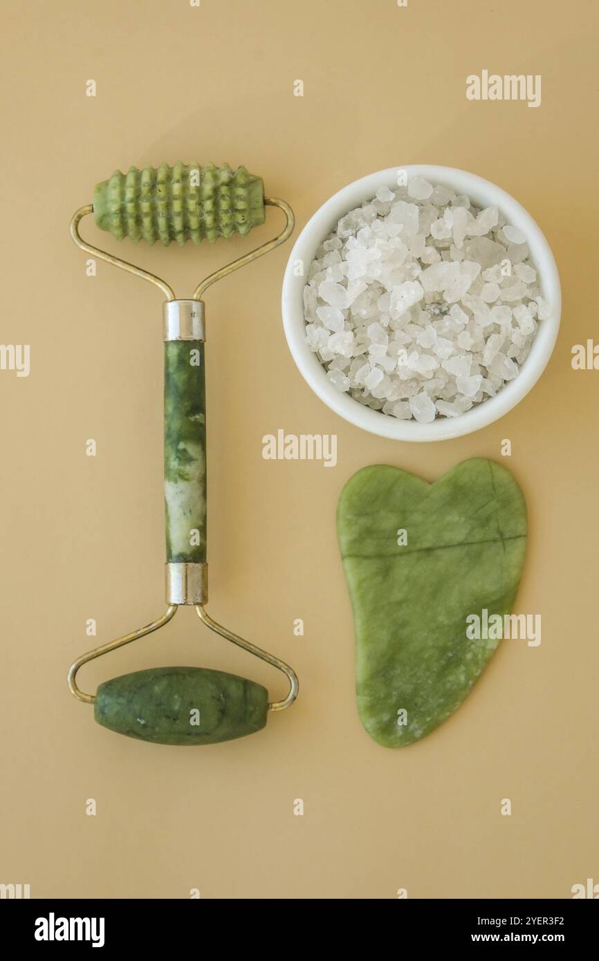 Gesichtswalzen Gouache Massagegerät Scraper, aus natürlichem Amethyst. Selbstpflege-Set. Home Spa-Produkte auf neutralem beigen Hintergrund. Gesichtsbehandlungen Stockfoto