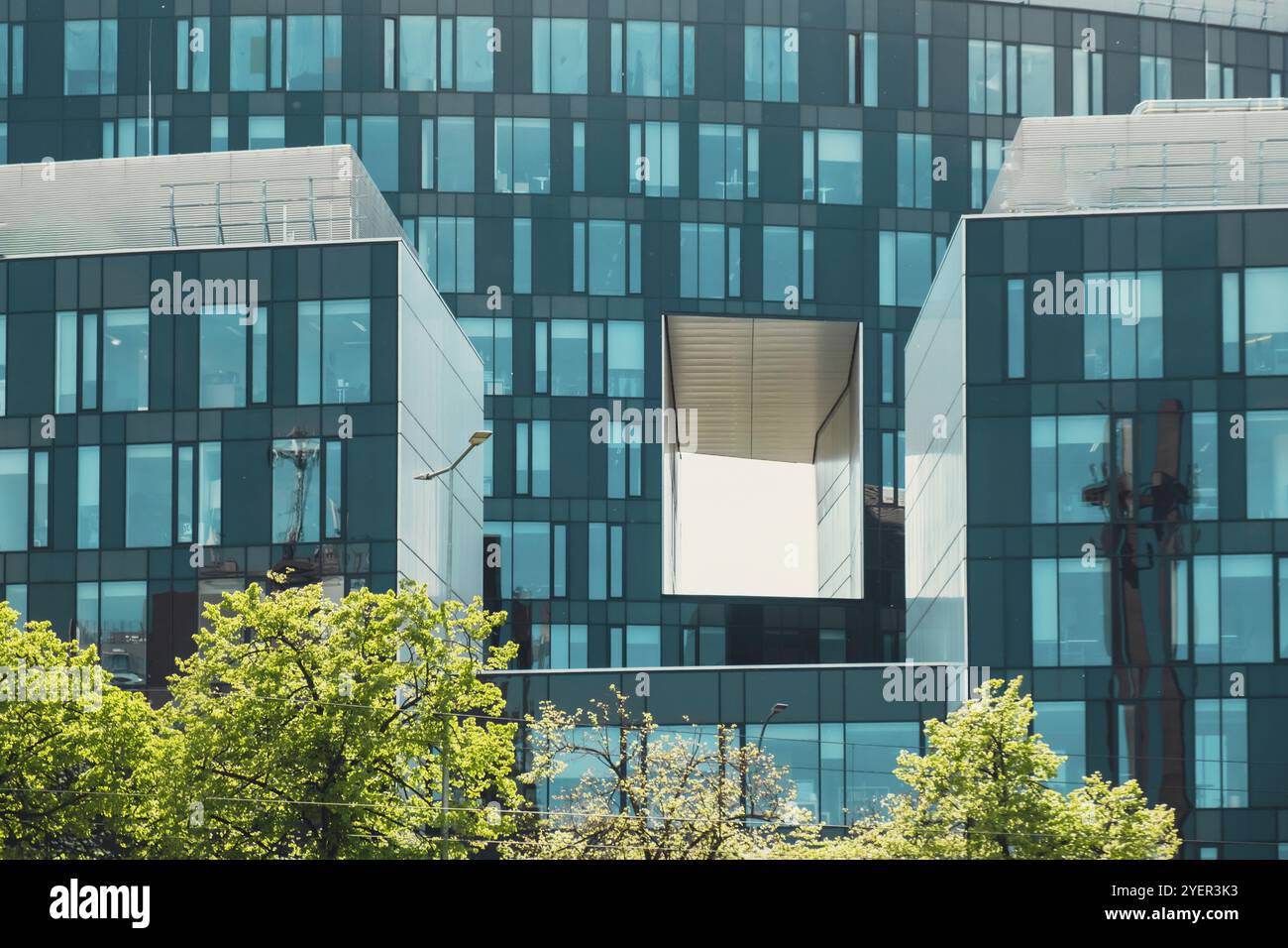 Moderne Glasfassade der Bürogebäudearchitektur. Abstraktes Gebäude mit Fenstern und grünen Bäumen davor. Modernes Hochhaus Stockfoto