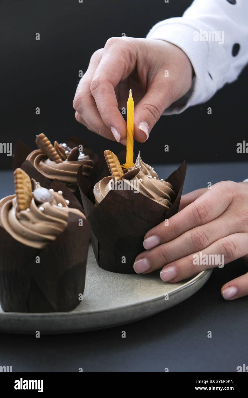 Weibliche Hände, die leckere Cupcakes aus Schokolade mit Creme auf dunklem Hintergrund herstellen. Drei Schokoladenmuffin. Geburtstagskuchen Party Vorbereitung. Hausgemachte Schokolade Stockfoto