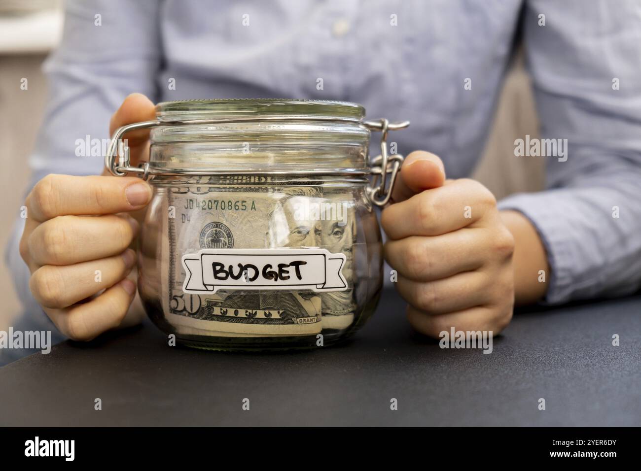 Unerkennbare Frau, die Spargeld in einem Glasgefäß hält, gefüllt mit Dollarscheine. BUDGET-Transkription vor dem Glas. Verwalten persönlicher Finanzen Stockfoto