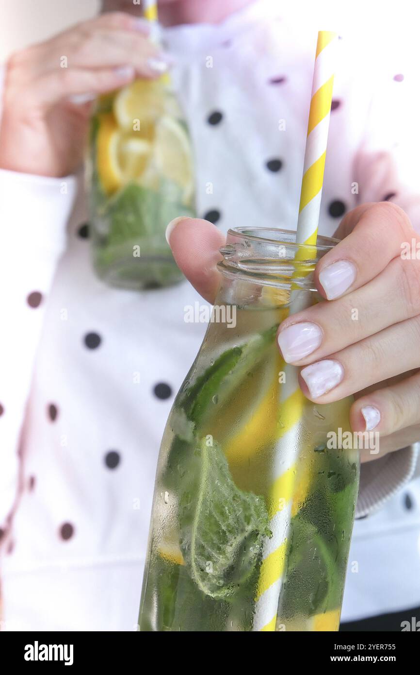 Weibliche Hand hält Mojito erfrischenden Cocktail mit Öko-Papier Trinkhalm, Alkoholgetränk. Limonade mit Zitronen- und Minzblättern. Sommerliche Erfrischung de Stockfoto