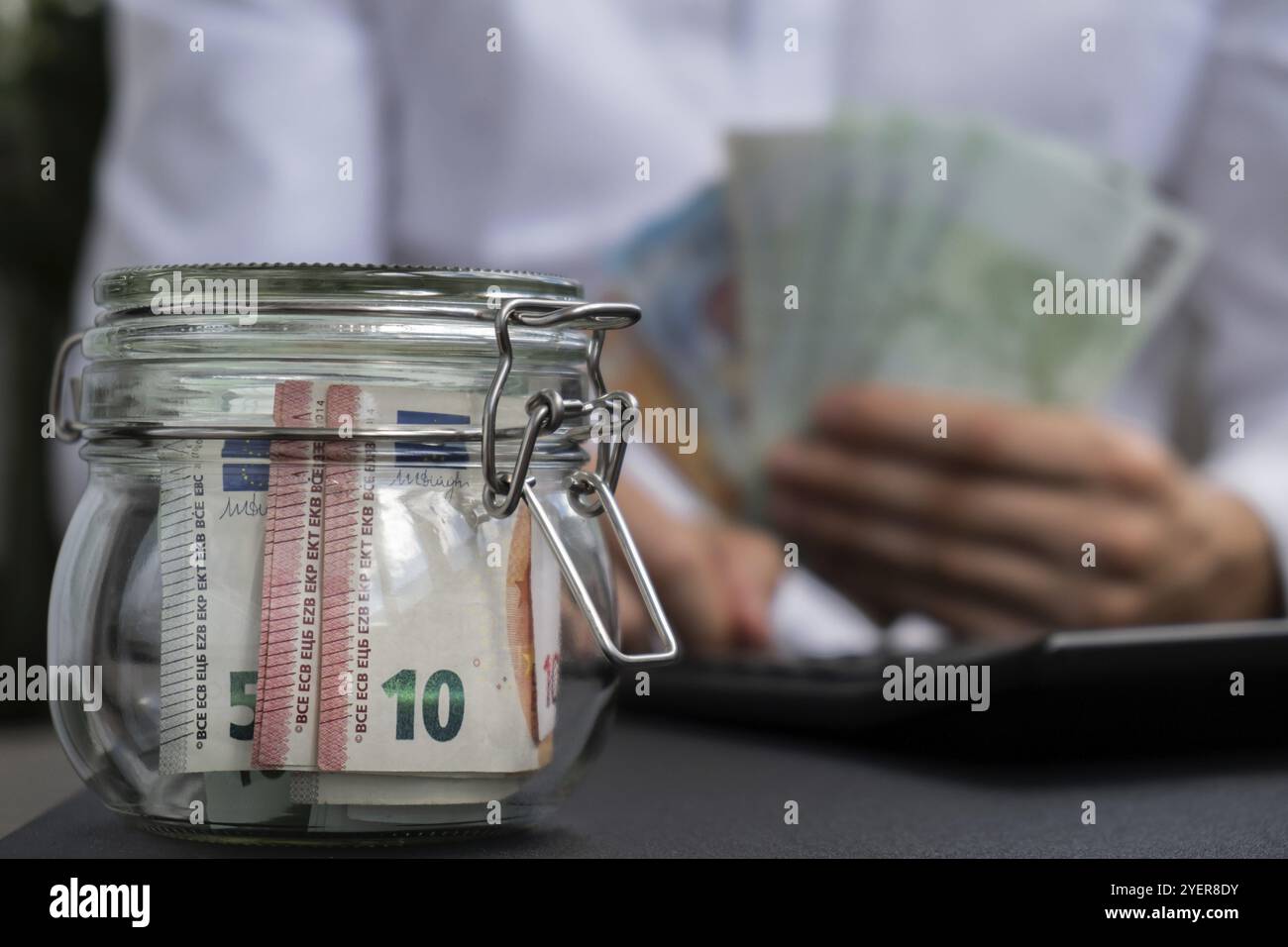 Euro-Banknote Spart Geld Im Glasgefäß. Unerkennbarer Mann moderat Verbrauch auf Rechner und Wirtschaft Geld sammeln Tipps Business Finance Fuß Stockfoto