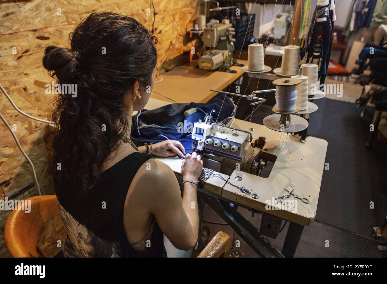 Ein Blick über die Schulter eines langen schneiderin bei der Arbeit im Studio, saß am Schreibtisch, die altmodische umstechen Maschine mit weißem Faden Schieber Stockfoto