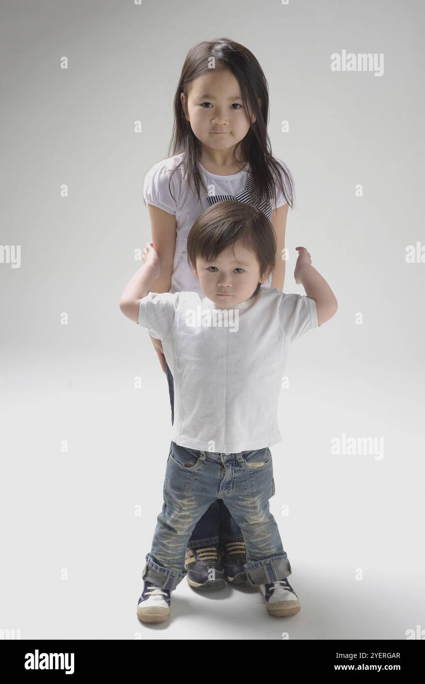 Zweijährige, die senkrecht auf ihrer sechsjährigen Schwester steht Stockfoto