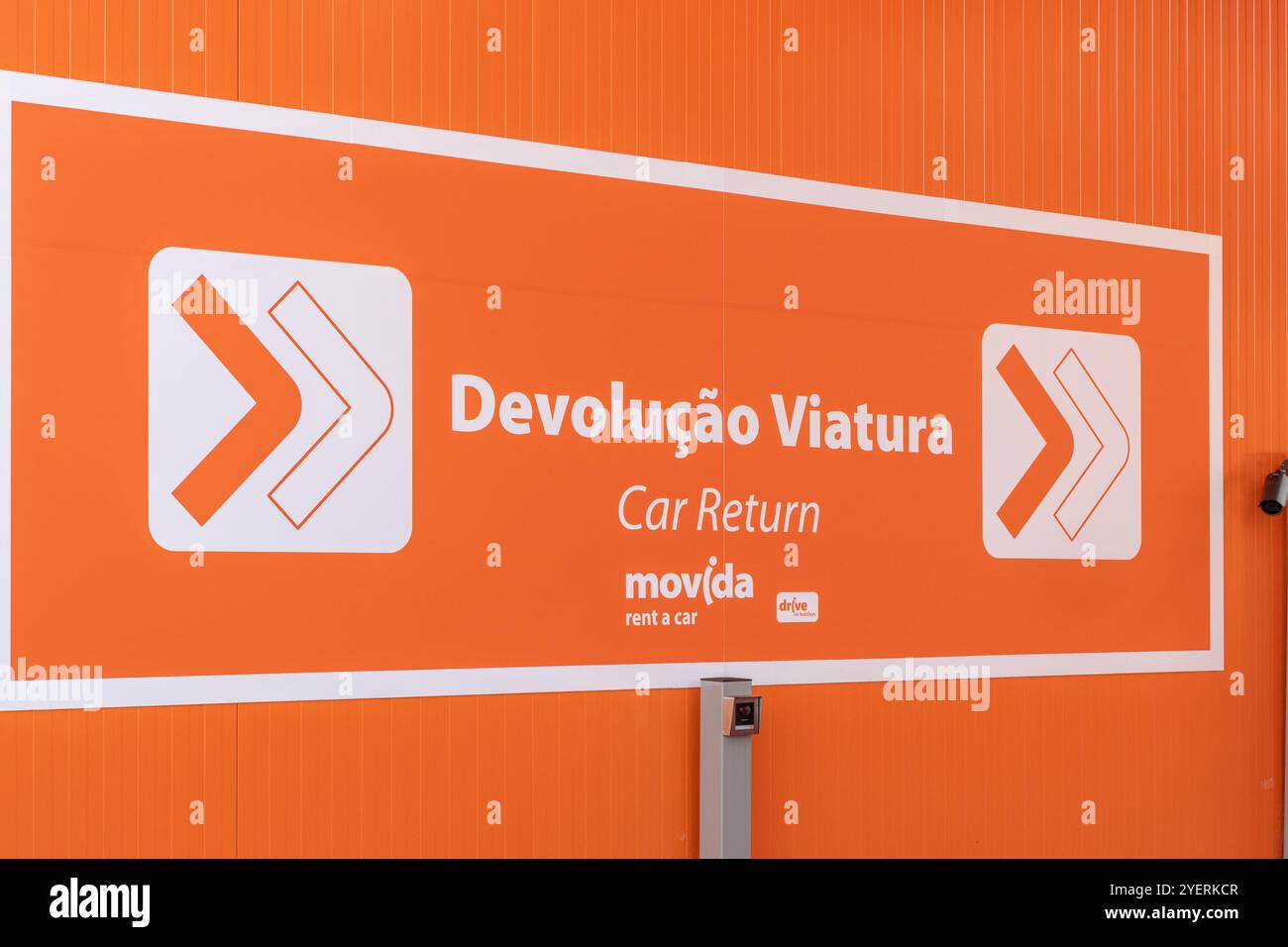 Orangefarbenes Schild, das den Abgaberaum für Movida-Mietwagen anzeigt, mit weißen Pfeilen und portugiesischem und englischem Text Stockfoto