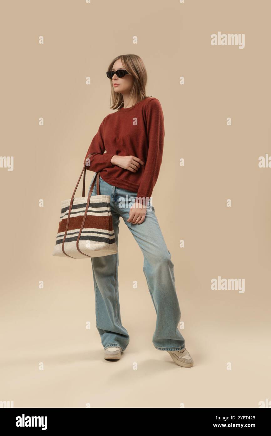 Serie von Studiofotos von Frauen im klassischen Herbst-Freizeitoutfit – blaue Jeans, brauner Pullover, Sonnenbrille und große Tragetasche. Stockfoto