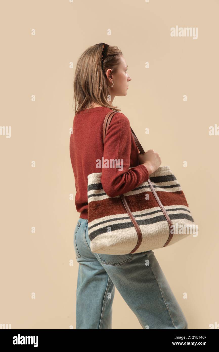 Serie von Studiofotos von Frauen im klassischen Herbst-Freizeitoutfit – blaue Jeans, brauner Pullover, Sonnenbrille und große Tragetasche. Stockfoto