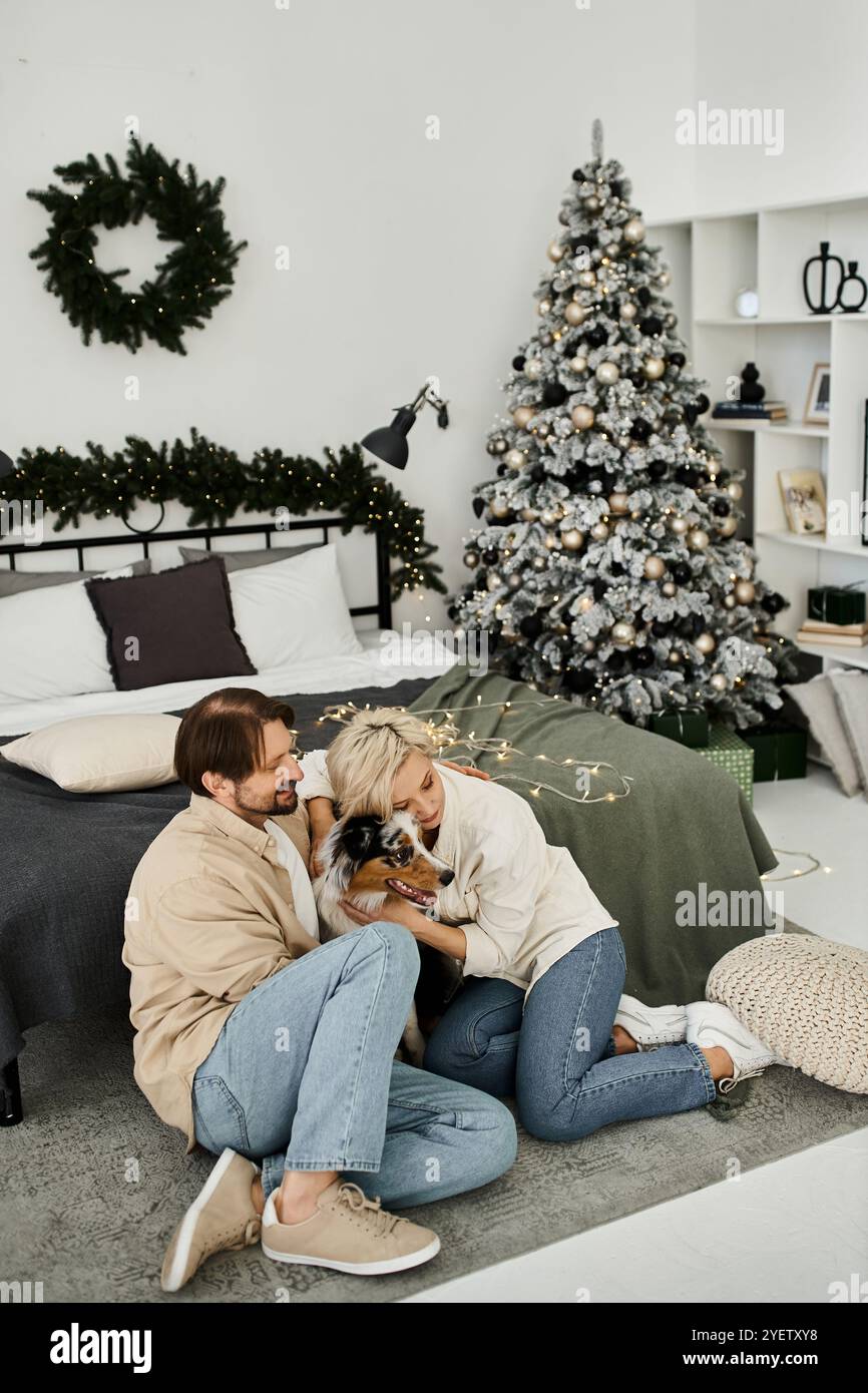 Ein Paar entspannt sich zu Hause mit seinem Hund, umgeben von Weihnachtsdekoration und einem warmen Ambiente. Stockfoto