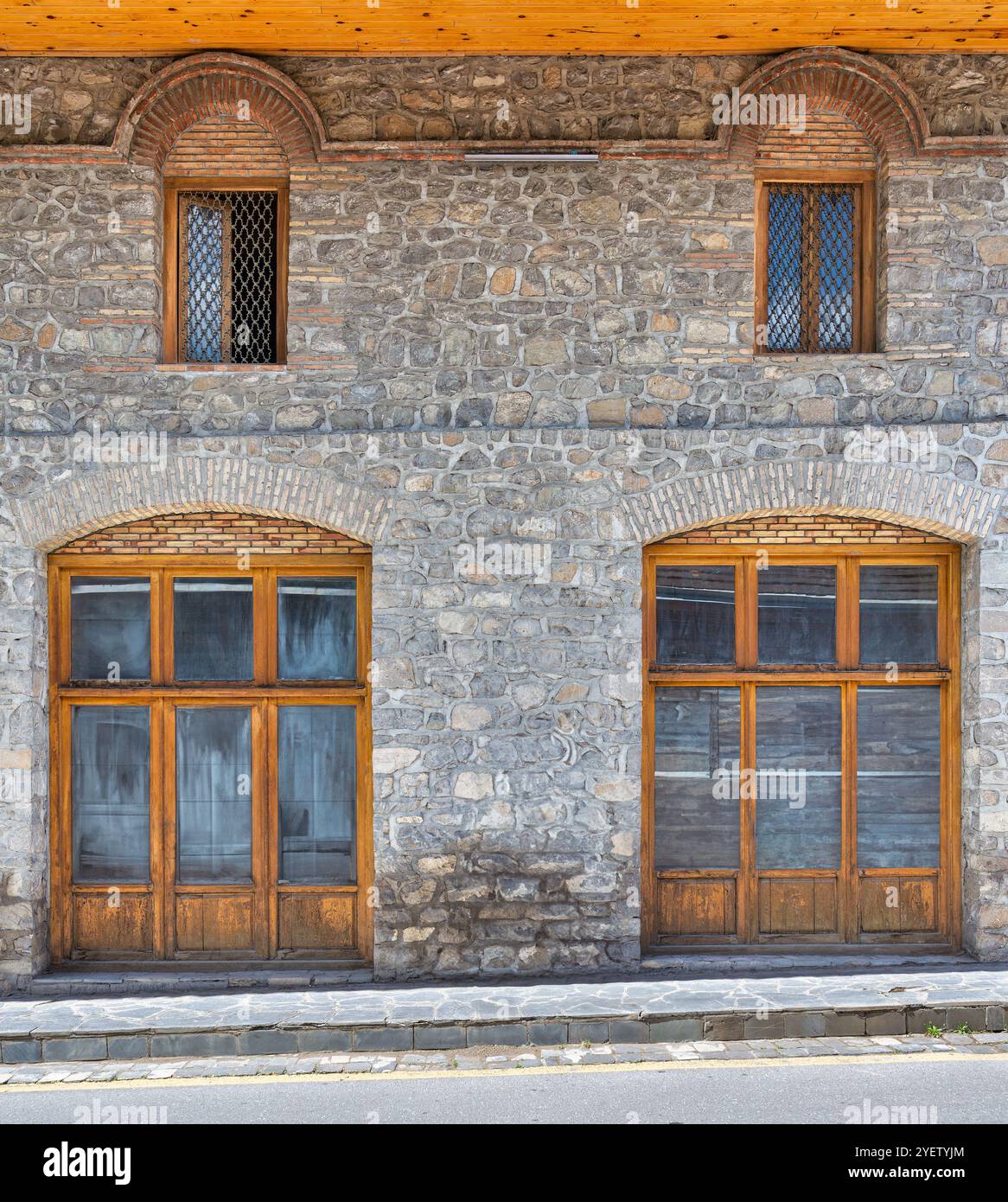Das rustikale Steingebäude verfügt über große Holzfenster, die die Handwerkskunst der alten Architektur in einem ruhigen Dorf hervorheben. Die Struktur spiegelt einen zeitlosen Charme wider Stockfoto