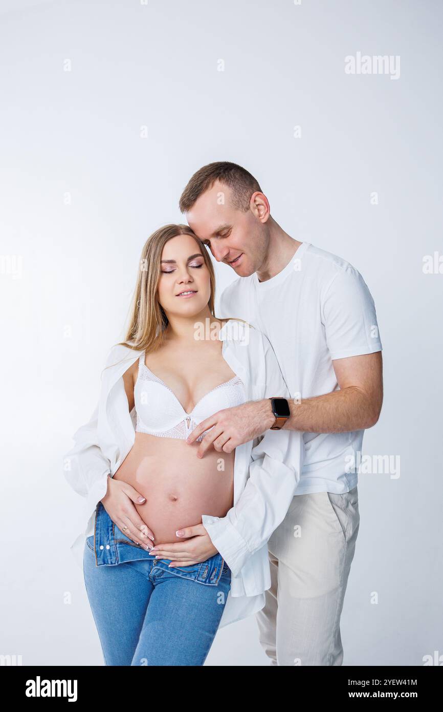 Ein Mann umarmt eine schwangere Frau und streichelt ihren Bauch, ein glückliches junges Paar ist schwanger. Stockfoto