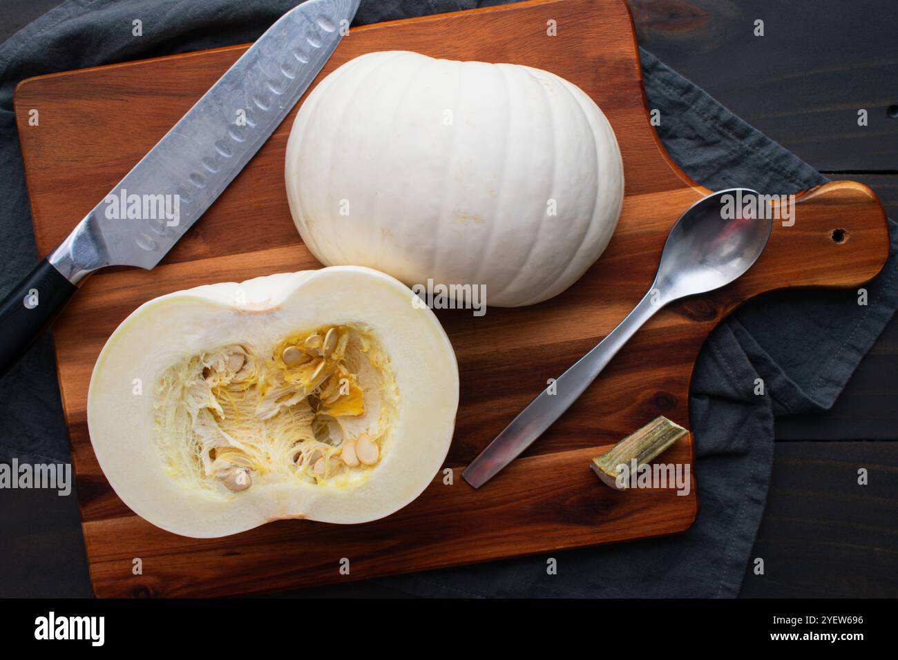 Halbierter White Pie Kürbis auf einem Schneidebrett: Vorbereiten, um die Samen und das Fruchtfleisch von einem Schneeballkürbis mit einem Kochmesser und Löffel zu entfernen Stockfoto