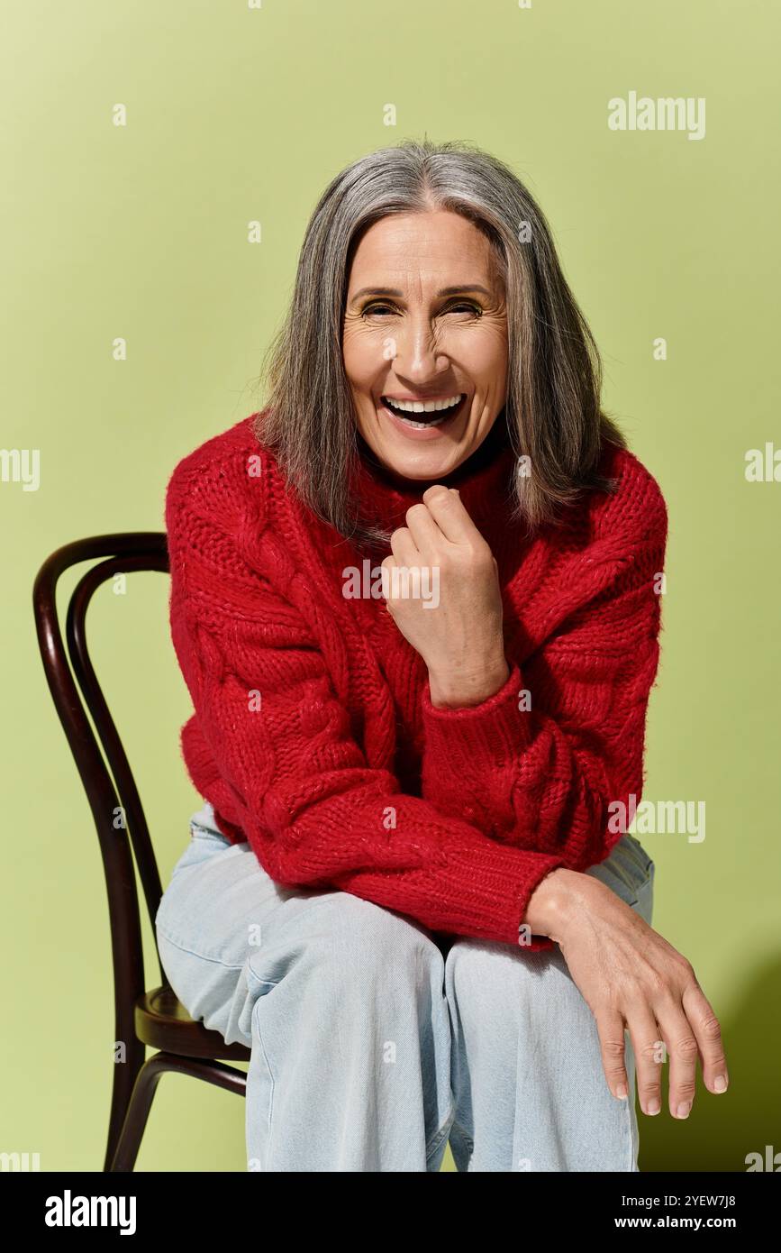 Eine fröhliche reife Frau mit grauem Haar lächelt hell, warm in einem roten Pullover an einem kühlen Tag gekleidet. Stockfoto