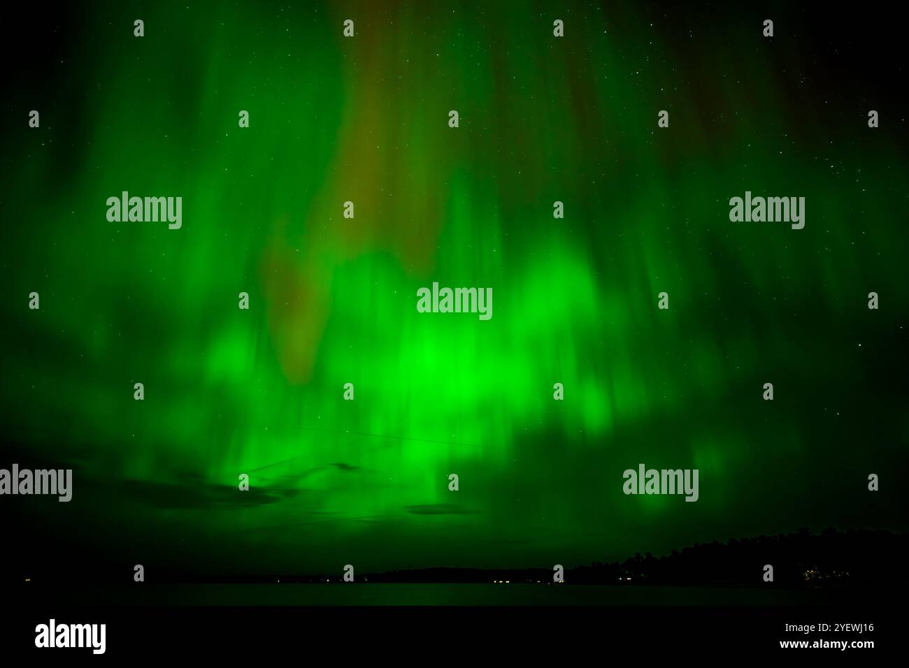 Leuchtende rote und grüne Auroras (Nordlichter) bemalen den Nachthimmel und schaffen eine faszinierende und surreale Atmosphäre über der Grand Traverse Bay, Michigan, Stockfoto
