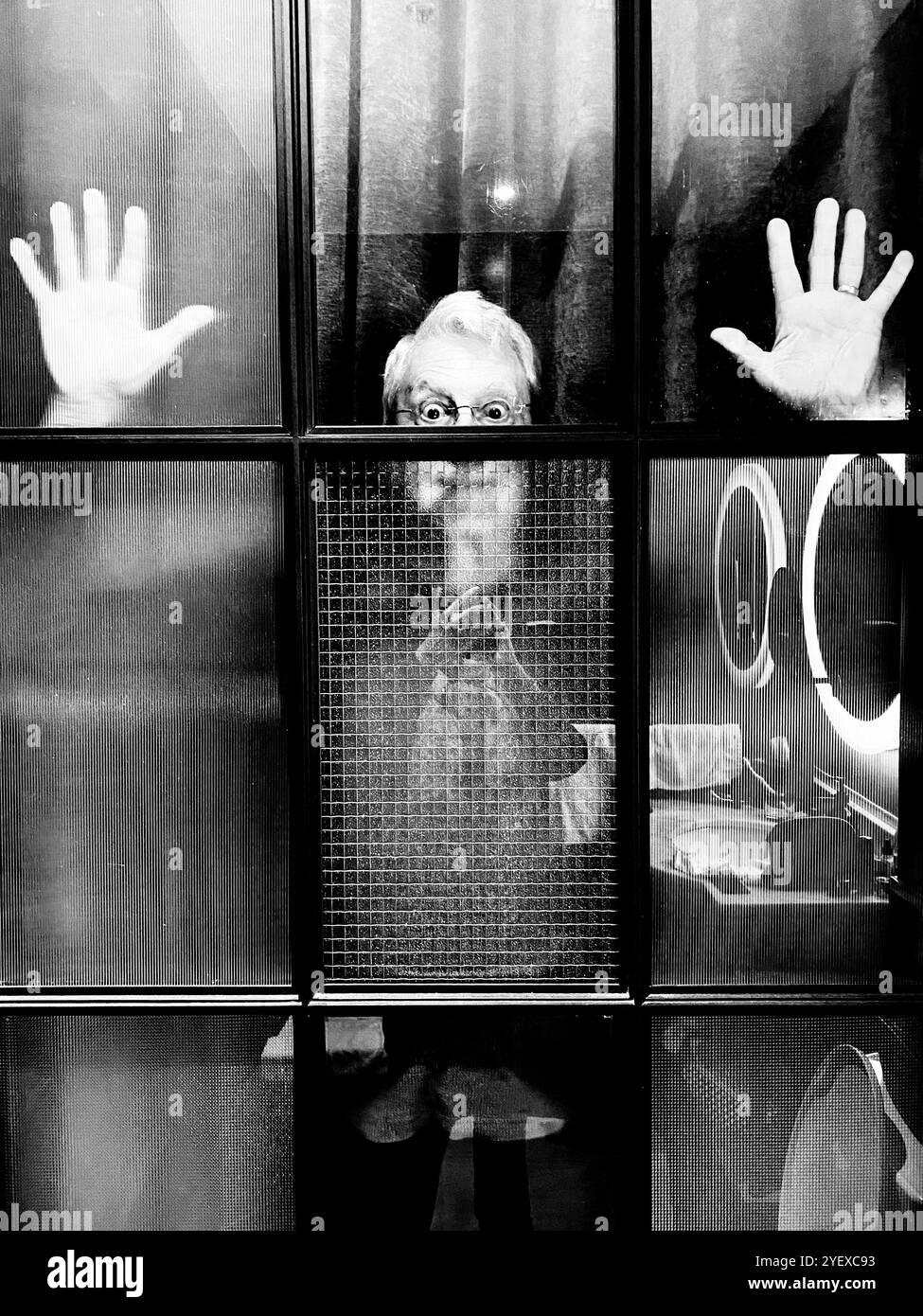 Ein Mann, der hinter eine verglaste Tür oder ein Fenster starrt und unglücklich aussieht. - Smartphone-aufgenommenes Stockfoto