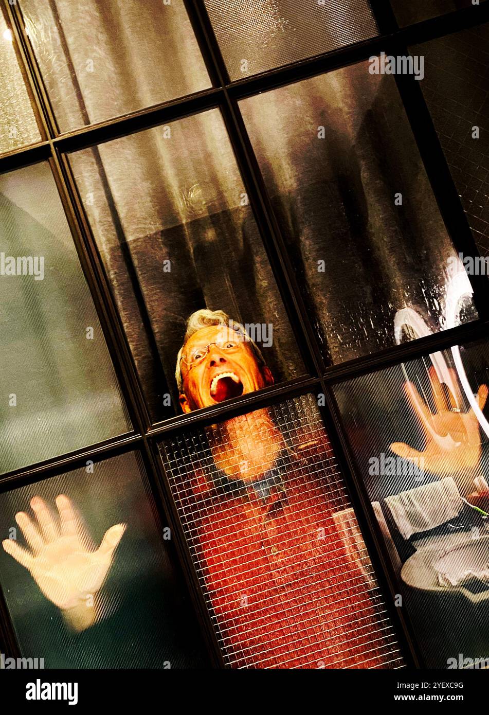 Mann, der hinter einer verglasten Tür oder einem Fenster schreiend mit Händen gegen das Glas gedrückt und unglücklich oder frustriert aussieht. - Smartphone-aufgenommenes Stockfoto