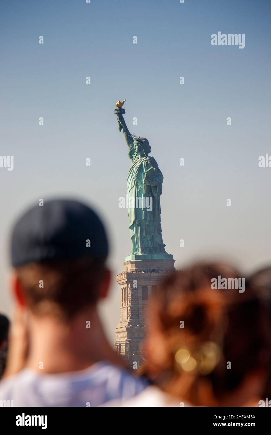 Die Freiheitsstatue steht hoch vor einem klaren blauen Himmel, von einer Menschenmenge auf der Fähre aus gesehen, die Freiheit und Demokratie symbolisiert Stockfoto