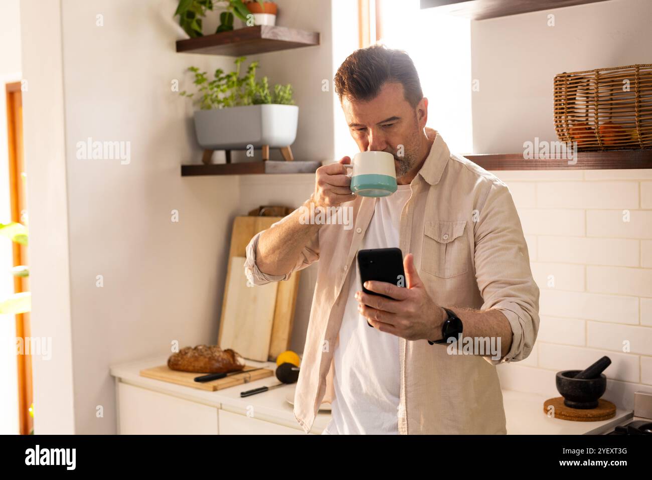 Senior Mann trinkt Kaffee und benutzt Smartphone in der gemütlichen Küche zu Hause Stockfoto