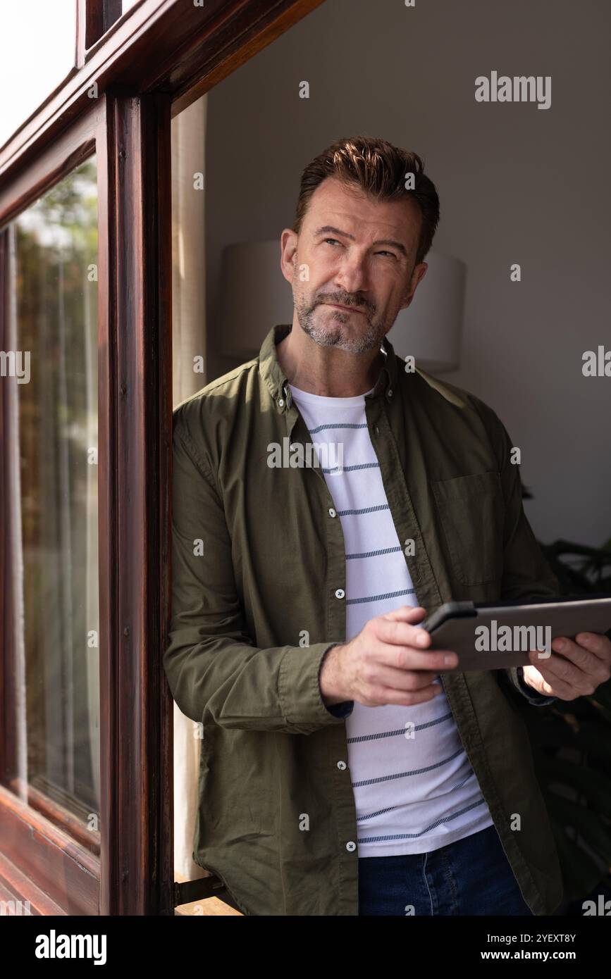 Senior-Mann mit Tablette, der nachdenklich aus dem Fenster zu Hause blickt Stockfoto