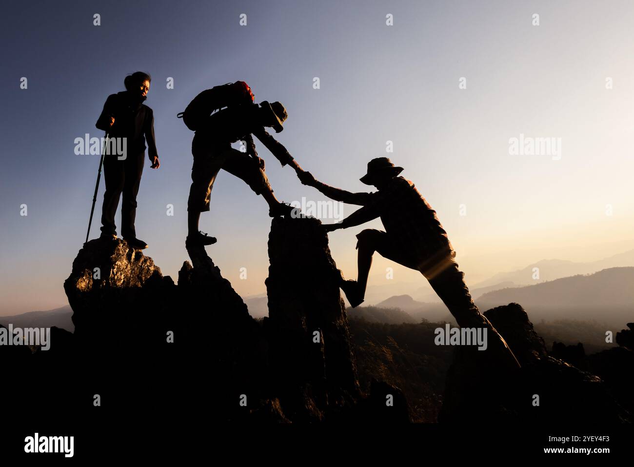 Silhouette von Wanderer, die Bergklippen hochklettern. Die Klettergruppe hilft sich gegenseitig, während sie bei Sonnenuntergang aufsteigt. Konzept von Hilfe und Teamarbeit. Stockfoto
