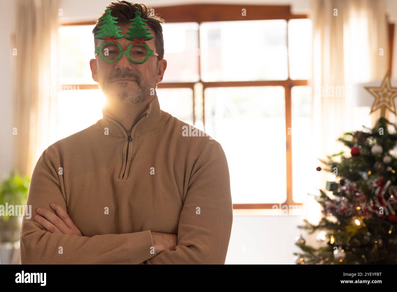 Seniorenmann mit festlicher Brille, der zuversichtlich neben dem Weihnachtsbaum steht, Kopierraum Stockfoto