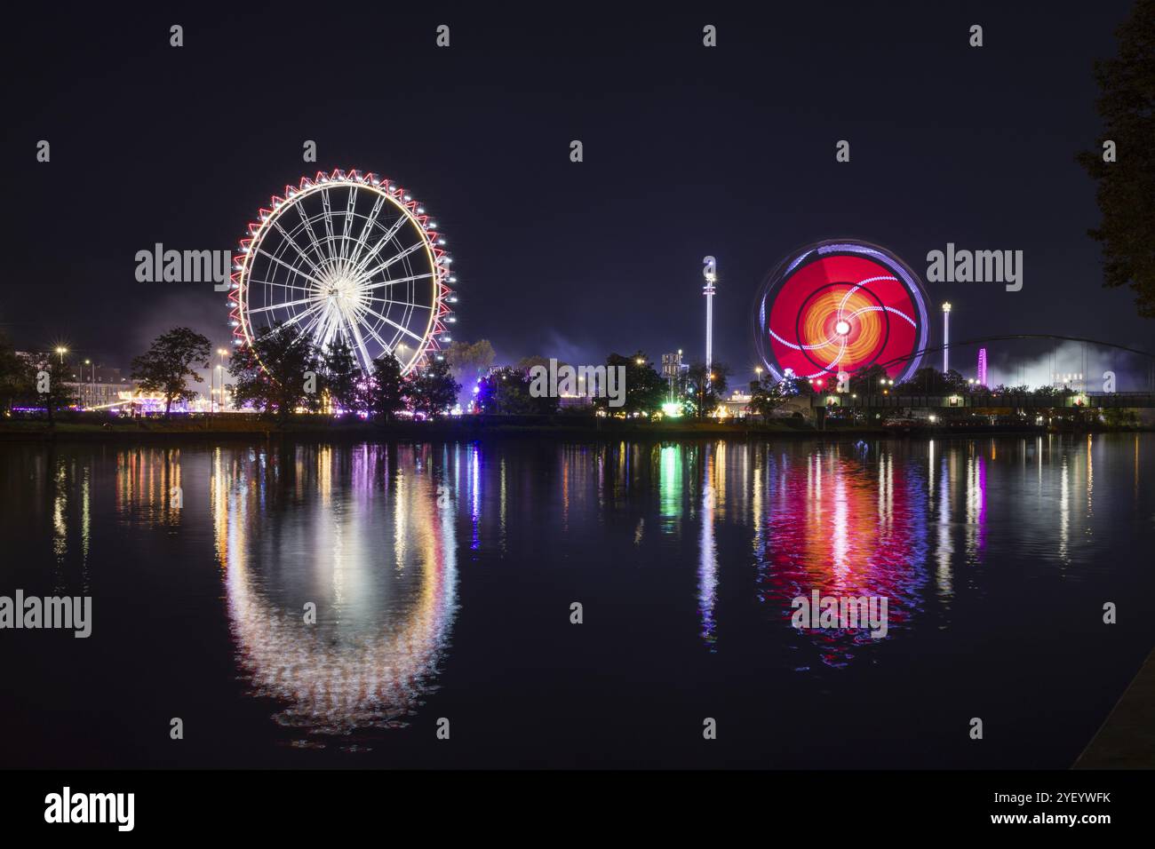 Stimmungsvolle Messe bei Nacht mit hell beleuchtetem Riesenrad und bunten Lichtern im Wasser, Cannstadter Volksfest, Stuttgart, Baden-Wuert Stockfoto