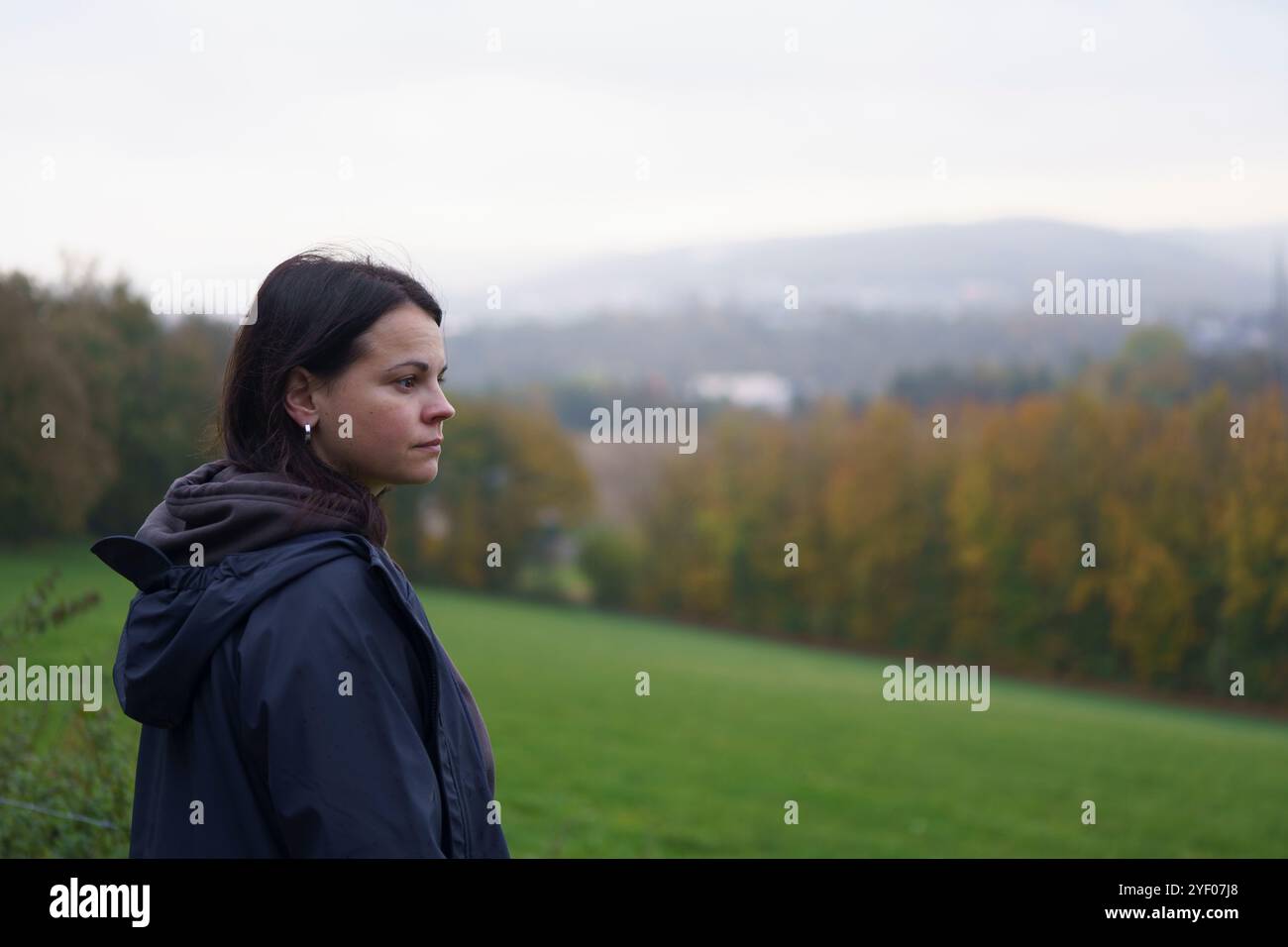 Ein Mädchen in einer Jacke, das seitlich zur Kamera steht, schaut nachdenklich in die Ferne vor dem Hintergrund eines unscharfen natürlichen Herbst-lan Stockfoto