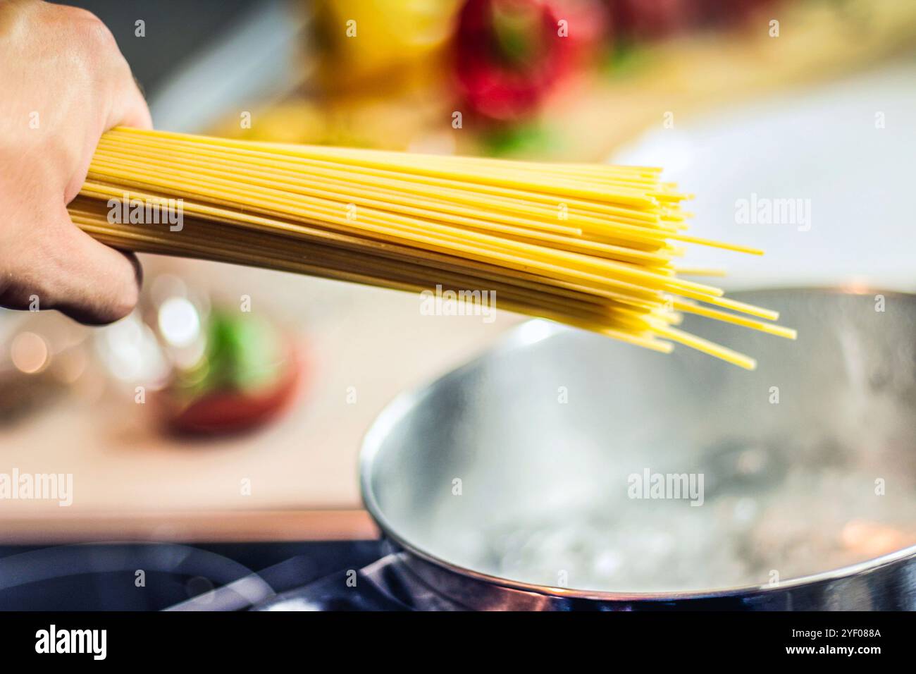 Nahaufnahme der Hand eines weißen Kaukasiers, der trockene Spaghettistangen in einen Topf voller kochendem Wasser steckt Stockfoto