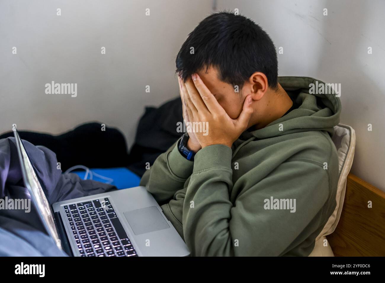 Ein besorgter Teenager sitzt auf seinem Bett und benutzt einen Laptop in Montrouge, Frankreich. Stockfoto