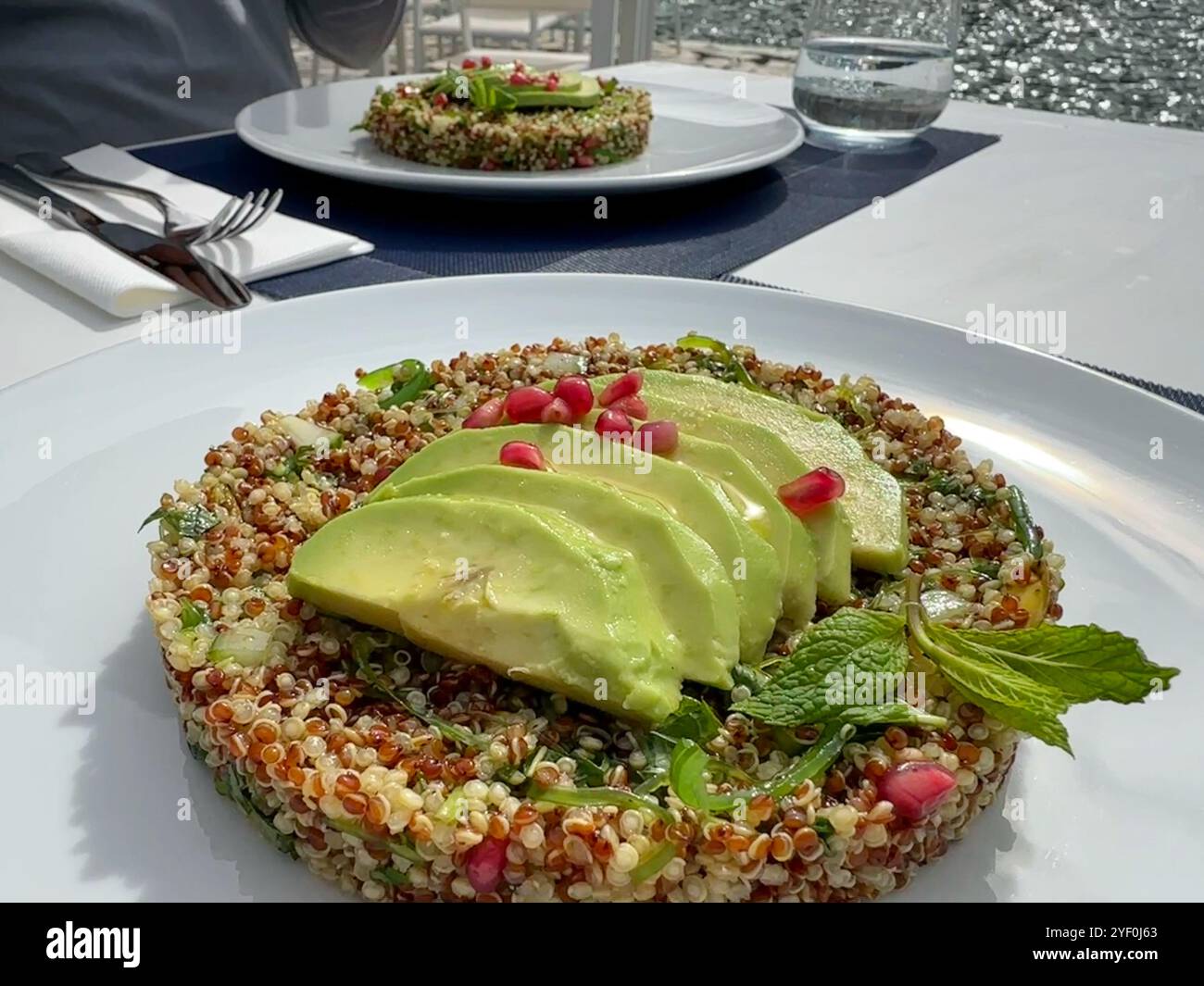 Nahaufnahme von zwei Quinoa-Salaten mit Avocado, Granatapfel, Pistazien und Minze auf einem Tisch am Meer Stockfoto