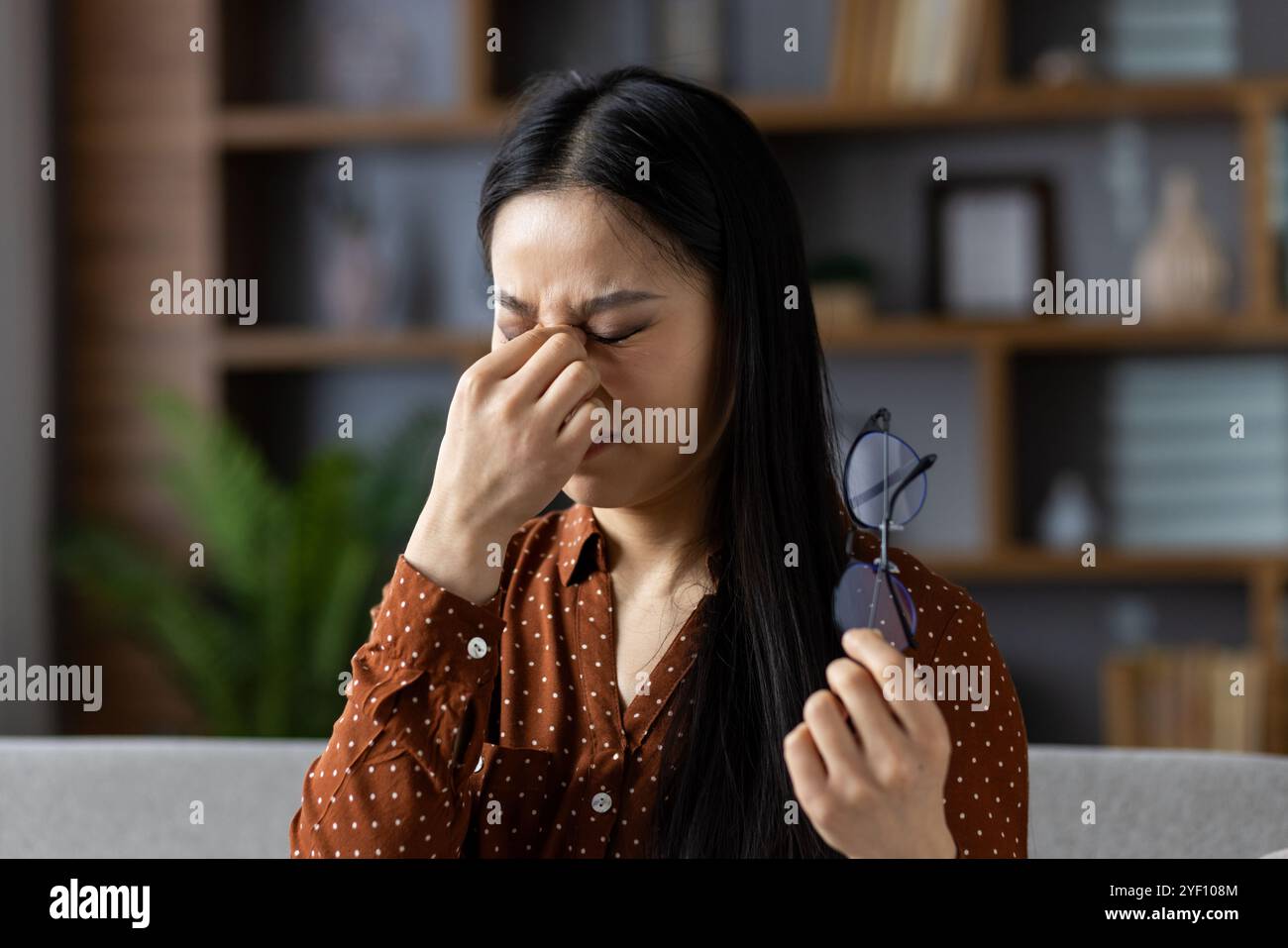 Asiatische Frau mit Augenanstrengung, Brille, Indoor Stress und Müdigkeit. Ihr Ausdruck zeigt Unbehagen und hebt Themen wie Müdigkeit, Kopfschmerzen, Stress hervor. Die gehaltene Brille bedeutet Abhilfe. Stockfoto