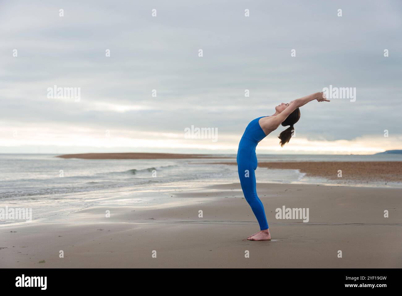 Sportliche Frau, die am Strand eine Dehnungsübung macht, Vorbereitung vor dem Schwimmen im Meer. Stockfoto