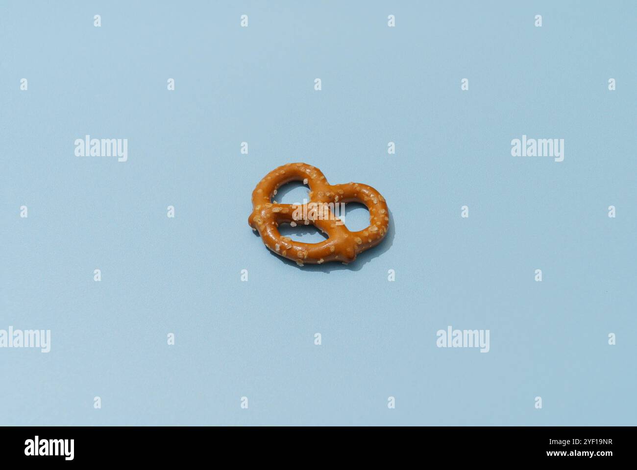 Eine einzelne braune Brezel mit Salzkristallen sitzt auf blauem Hintergrund. Die Brezel ist scharf, während der Hintergrund leicht verschwommen ist. Die Beleuchtung Stockfoto