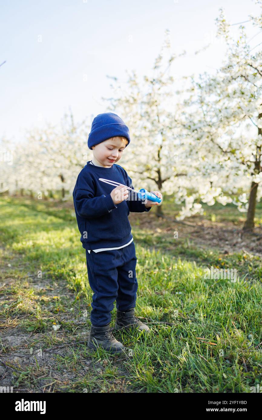 Ein dreijähriger Junge läuft mit Seifenblasen durch einen blühenden Garten. Fröhliches emotionales Kind läuft im Park. Seifenleisten für Kinder Stockfoto