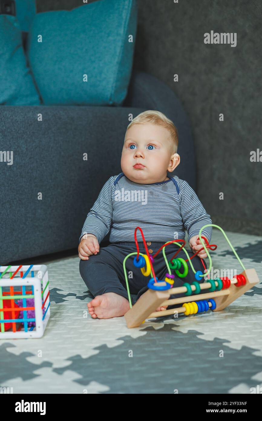 Ein Baby sitzt zu Hause auf dem Boden und spielt mit Spielzeug. Lernspielzeug für Babys. Ein Kind in einem Baumwoll-Body. Stockfoto