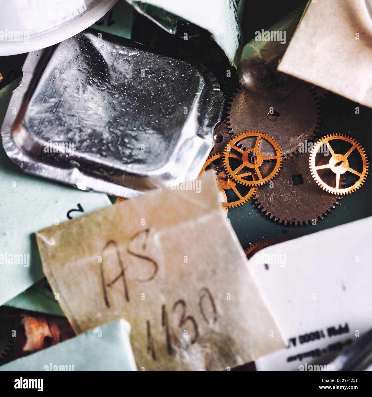 Verschiedene Uhrenkomponenten liegen auf der Werkbank verstreut, darunter Metallzahnräder, kleine Metallverpackungen und Etikettenpapier. Jedes Element spiegelt die Int. Stockfoto