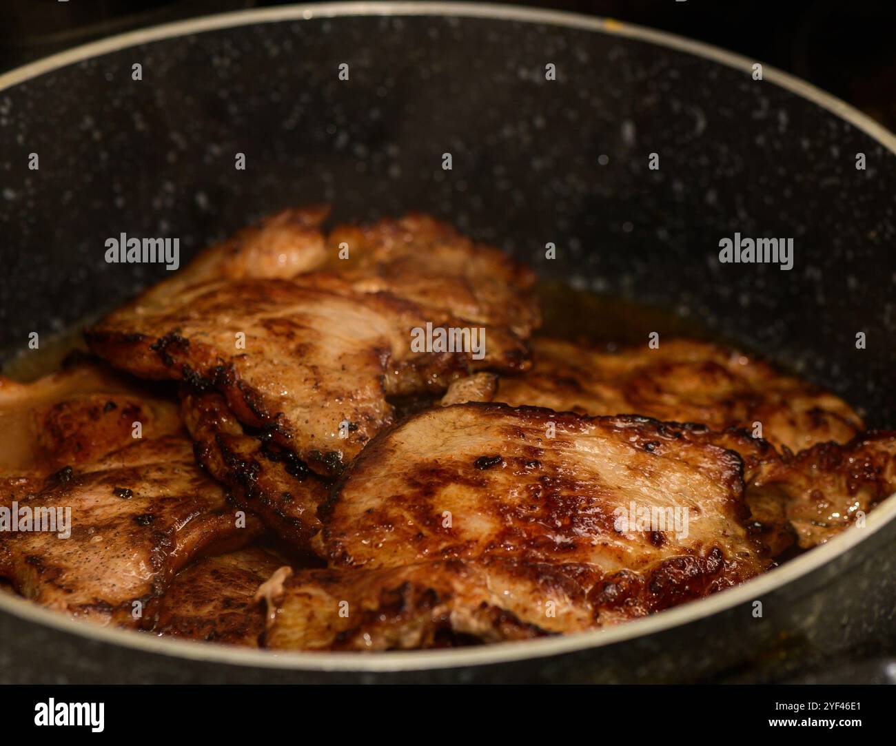 Saftige Schweinekoteletts braten in einer Pfanne an und geben unwiderstehliche Aromen in einer warmen, einladenden Küche ab. Stockfoto