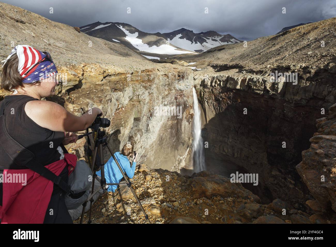 VULKAN MUTNOVSKY, HALBINSEL KAMTSCHATKA, RUSSLAND, 8. September 2015: Junge Fotografinnen fotografieren den Wasserfall auf dem Bergfluss in Gefahr Stockfoto